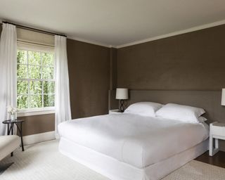 A bedroom with brown suede covered walls and white bed