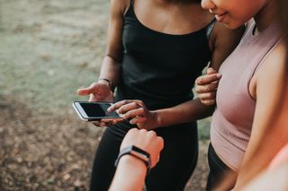 Female athletes check fitness tracker on smart phone