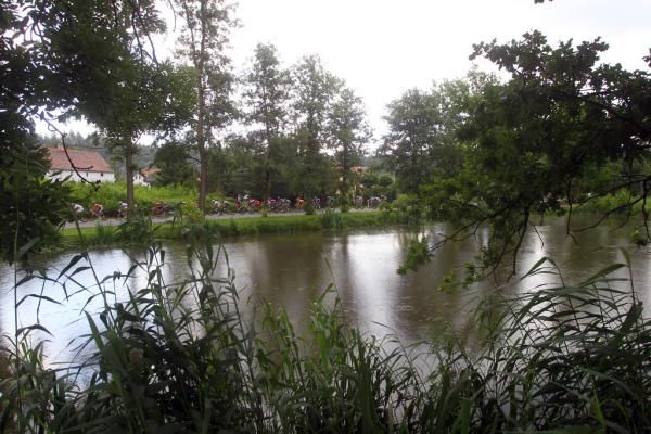 The peloton passes by a rain-speckled pond
