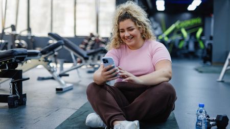 Woman sitting on mat in gym looking at her smartphone