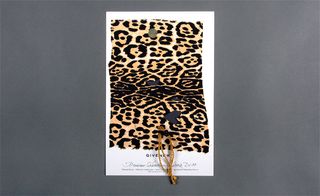 View of one side of ﻿Givenchy’s invitation pictured against a grey background. This side features leopard print, string and black text on a white card