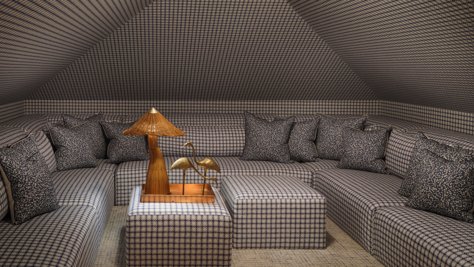 Media room with sloped ceilings, wraparound sofa and ottomans covered in the same blue geometric fabric.