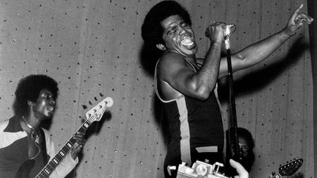 American soul singer and songwriter James Brown (1933-2006) performs live on stage with the J.B.'s, including bass guitarist Bootsy Collins on left and guitarist Catfish Collins (1943-2010) behind on right, in East Ham, London in March 1971