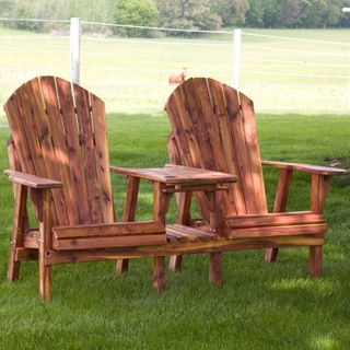 Two Adirondack chairs connected by wooden table set in grass