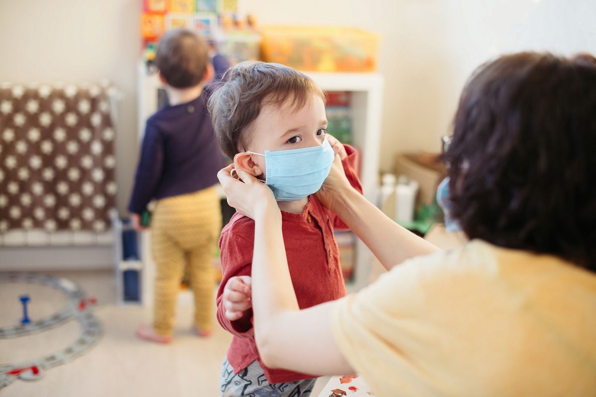 An adult puts a mask on a toddler.