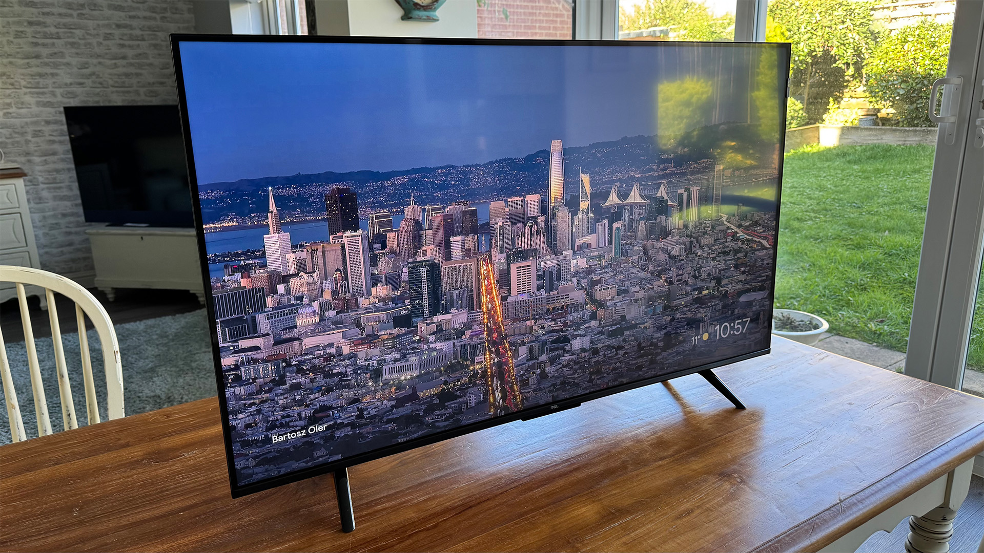 TCL P7K 43-inch TV on wooden dining table next to patio doors, on screen is cityscape