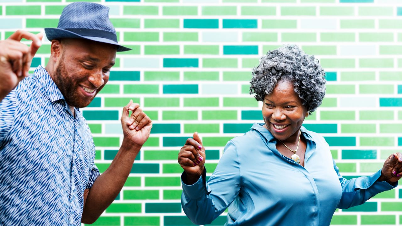 An older couple smile and laugh as they dance next to each other.