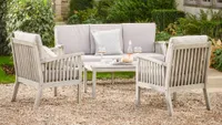 A wooden outdoor sofa and chair set on a gravelled patio