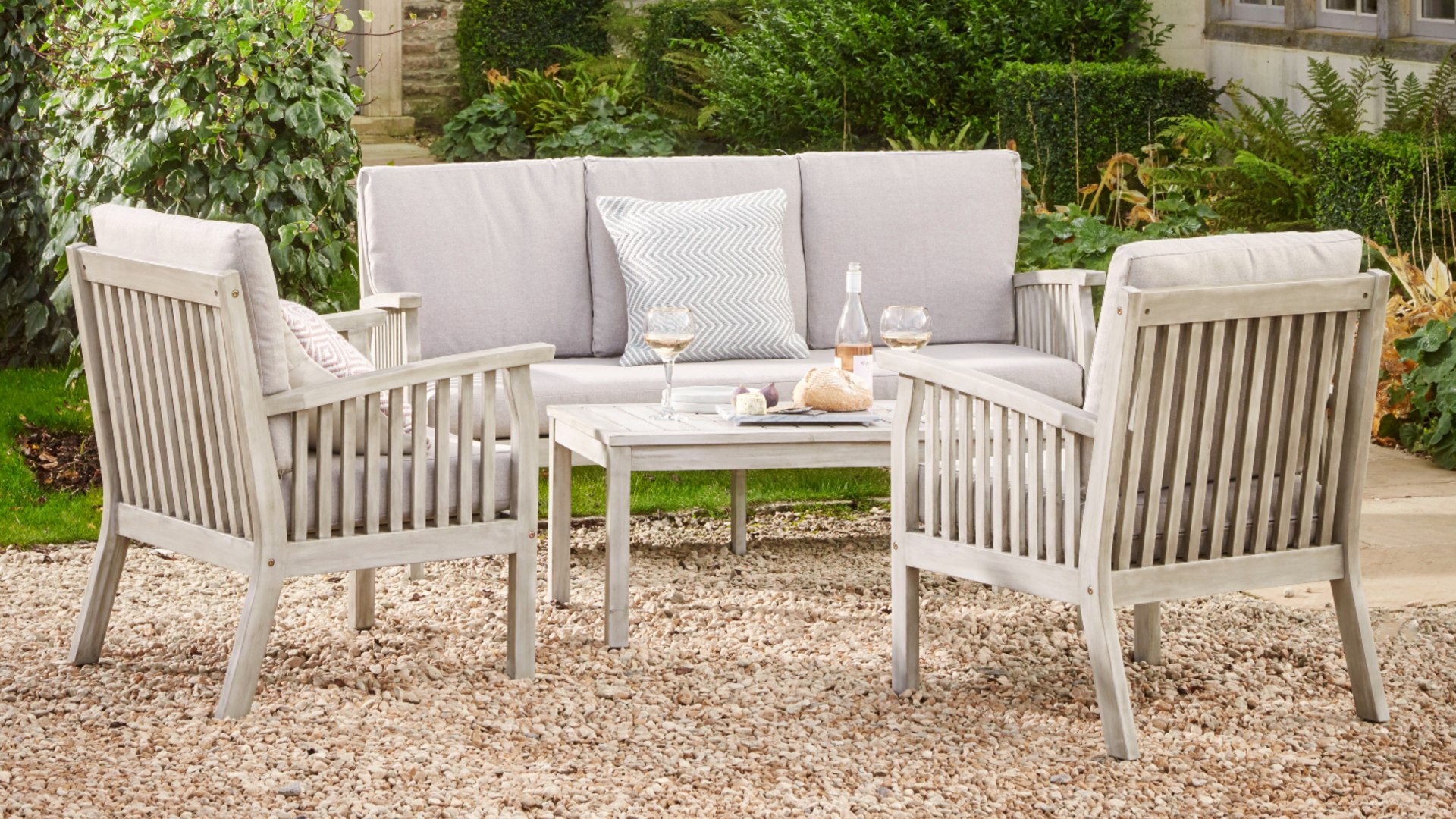 A wooden outdoor sofa and chair set on a gravelled patio