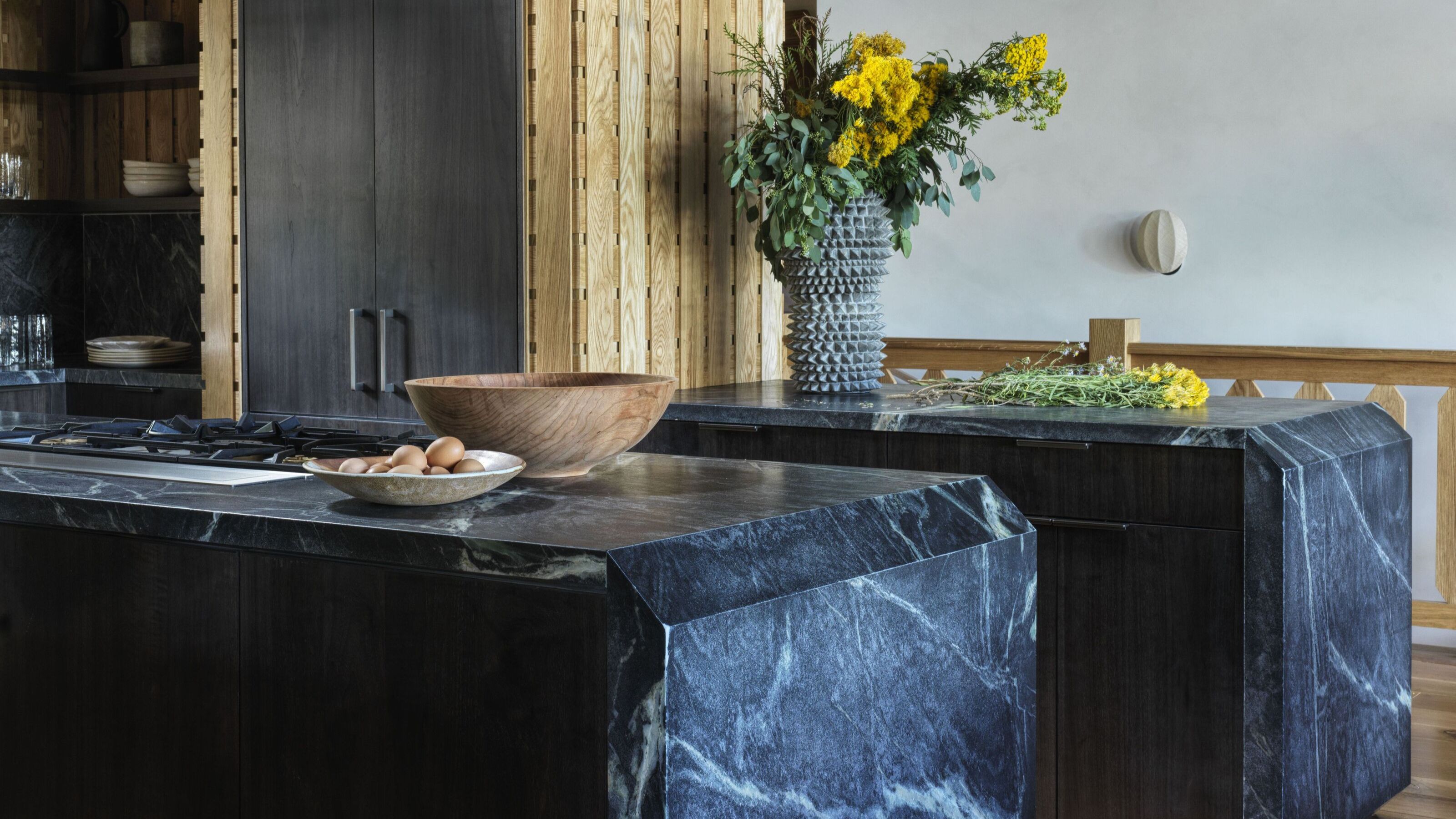Kitchen countertops with soapstone used on both counters. On one countertop there is also a stove with two bowls and on the other is a vase with flowers inside of it