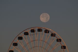 a full moon shines over a huge ferris wheel