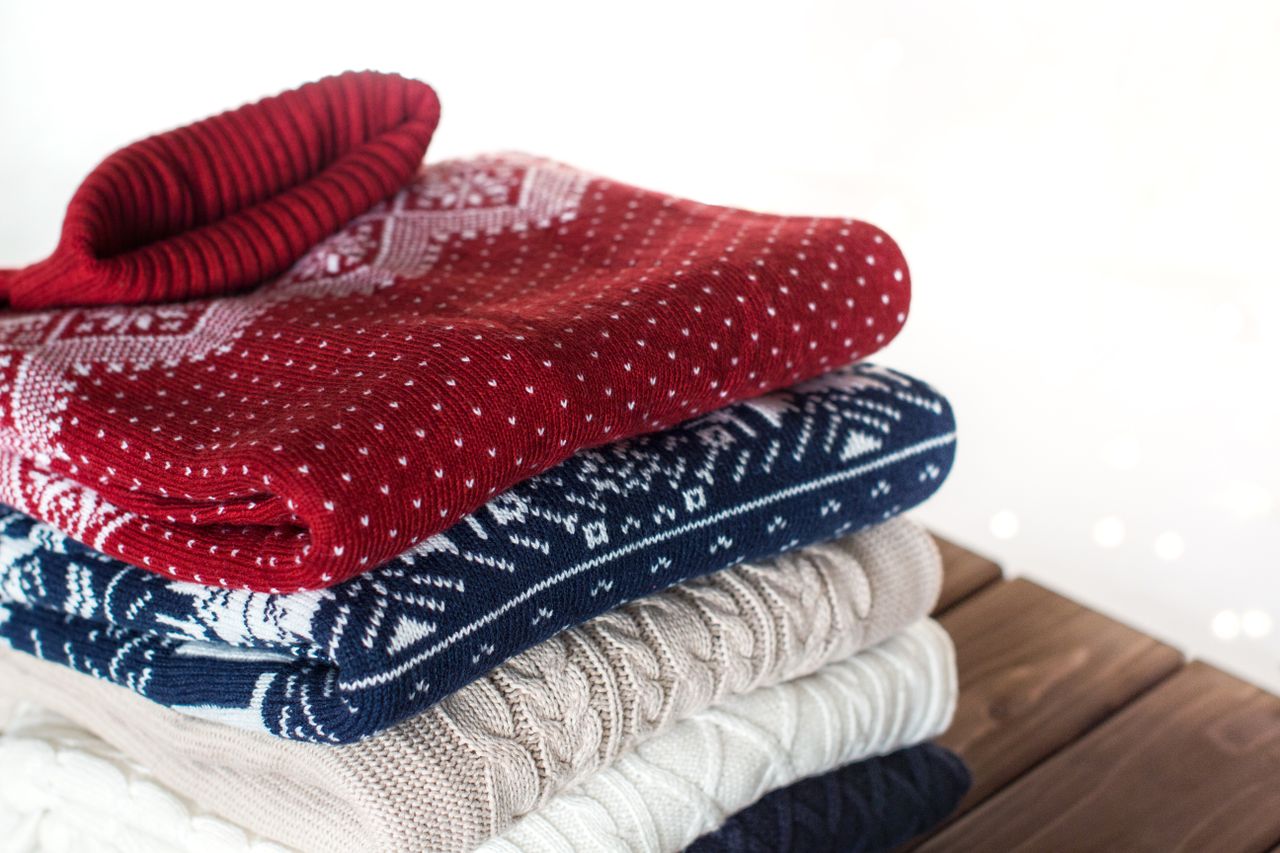 red, blue, white and beige christmas sweaters on dark brown wooden table