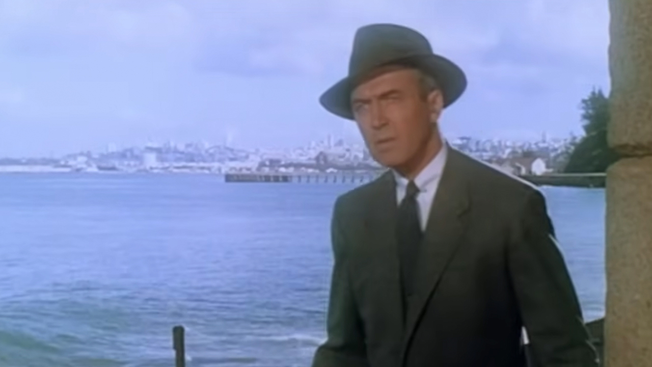 James Stewart in a suit and hat with the ocean and the skyline of San Francisco behind him in Vertigo