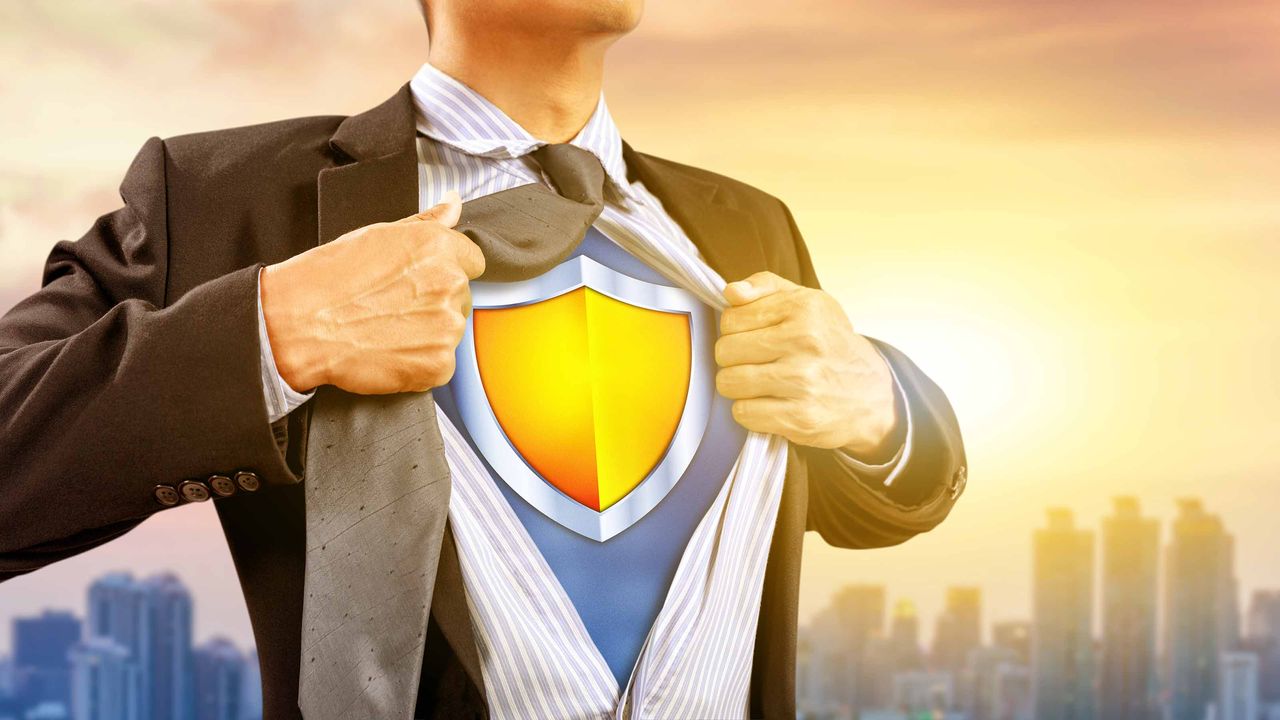 A businessman pulls apart a few buttons of his shirt to reveal a shield symbol underneath