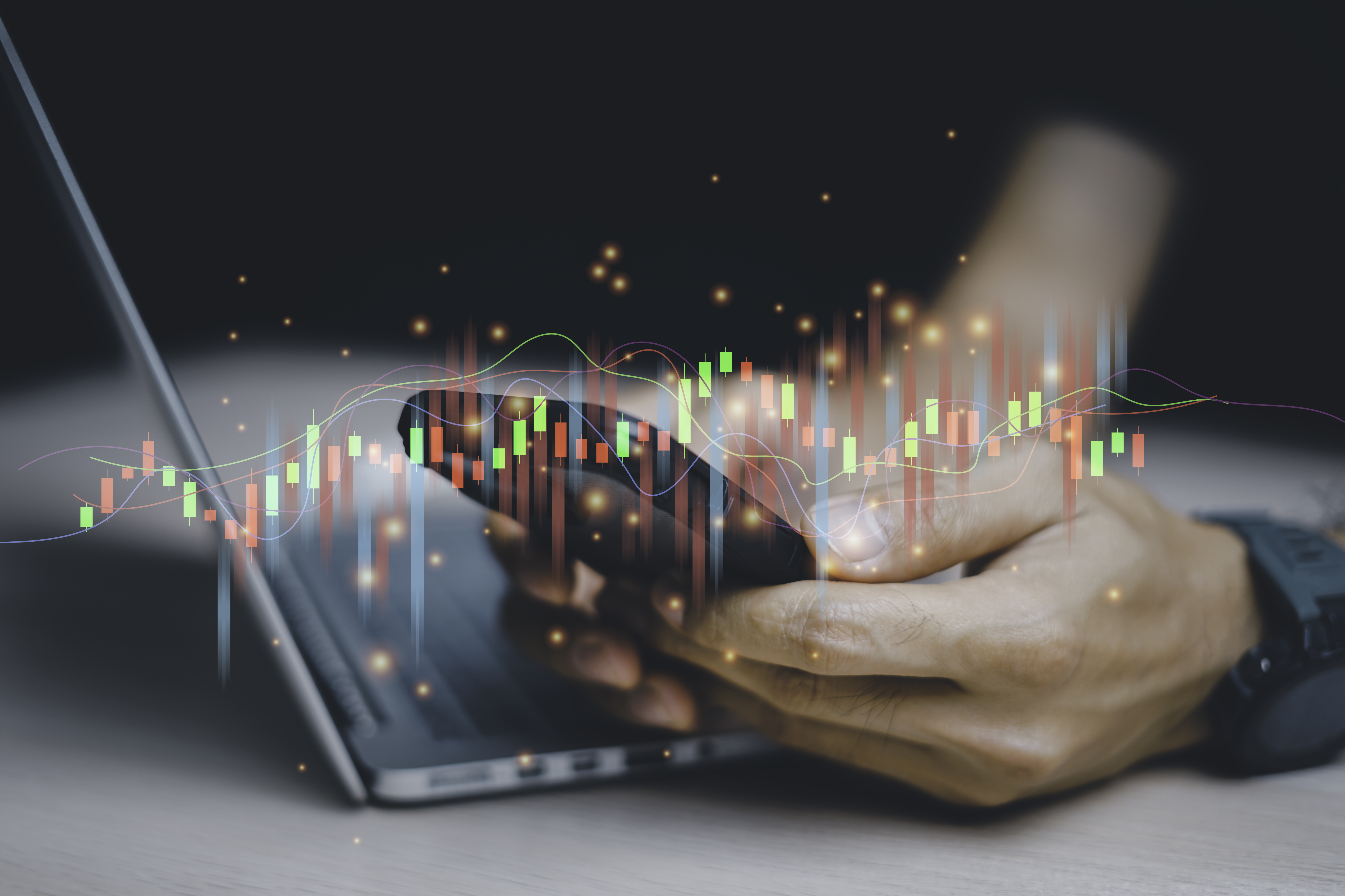 Person looks at phone and laptop and chart signifying investing over the top.