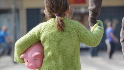 Child holding piggy bank and an adult’s hand