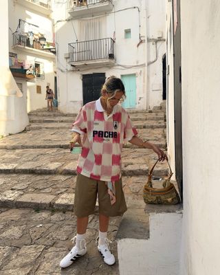 Sofia wears a red sports jersey, khaki shorts, white socks, and white adidas slip-on sneakers.