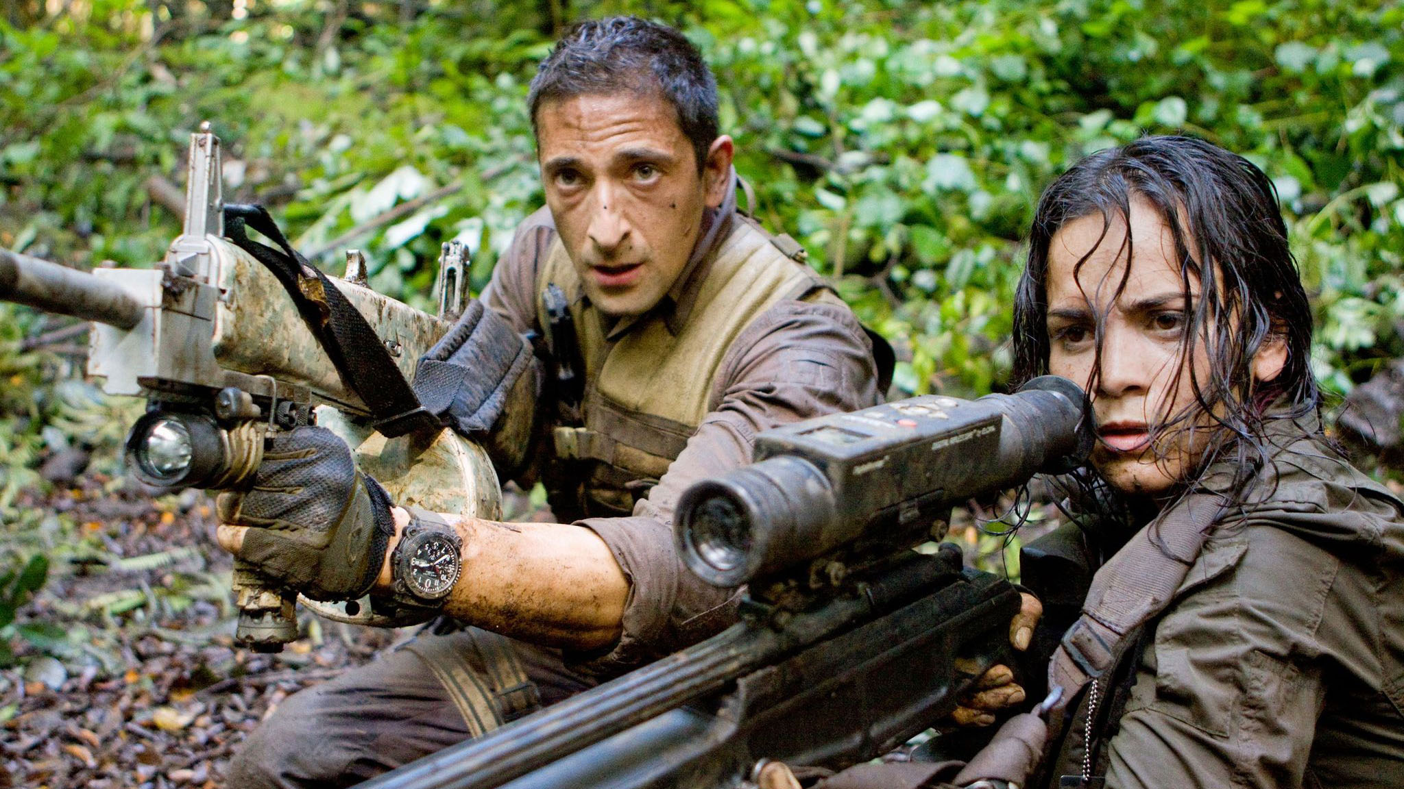 A still from the movie Predators in which Adrien Brody as Royce and Alice Braga as Isabelle hide in the jungle with guns