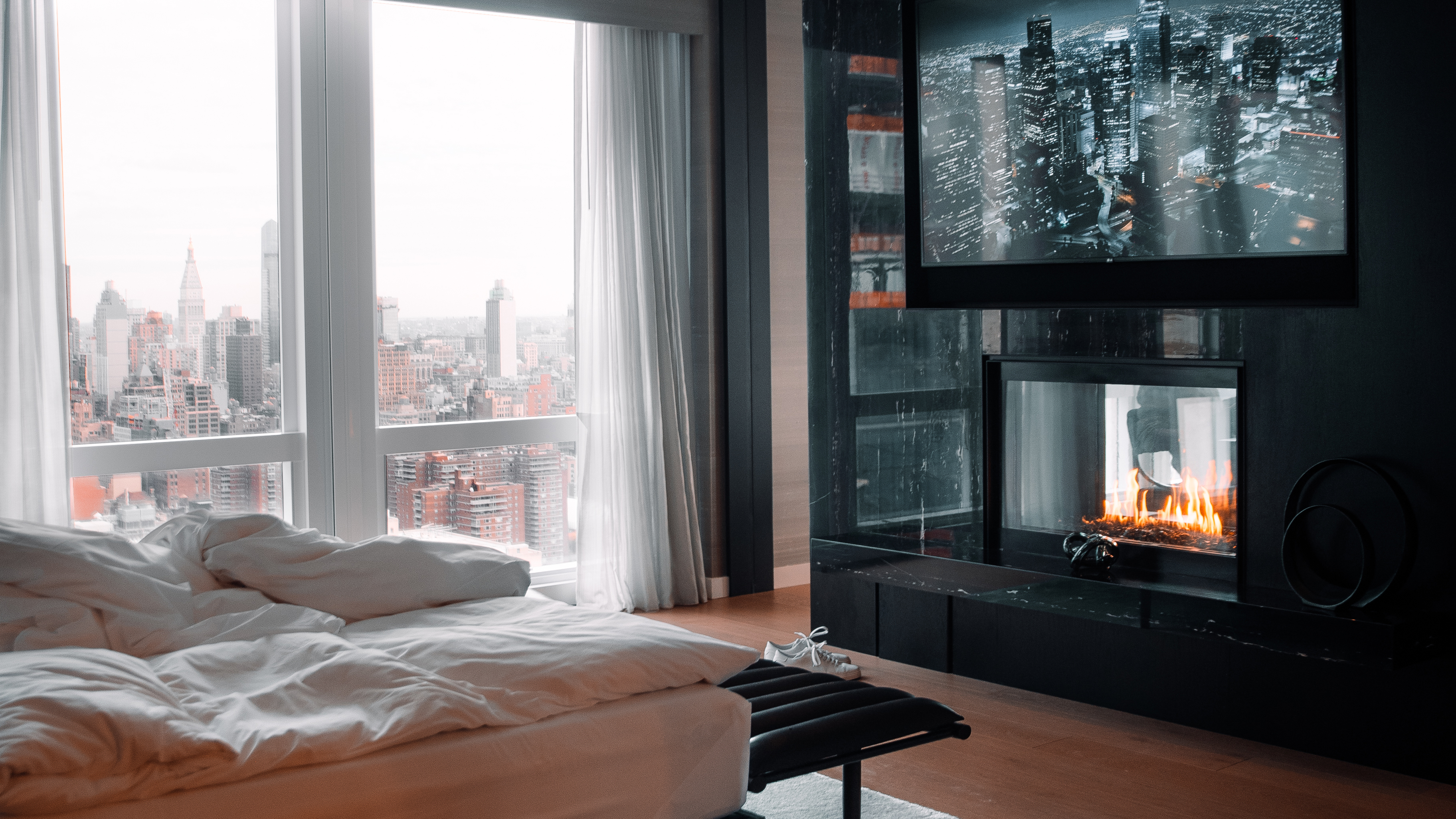 Equinox Hotels guest room in New York City, featuring the Equinox Sleep System on the left and a large-screen TV with a fireplace below it on the right