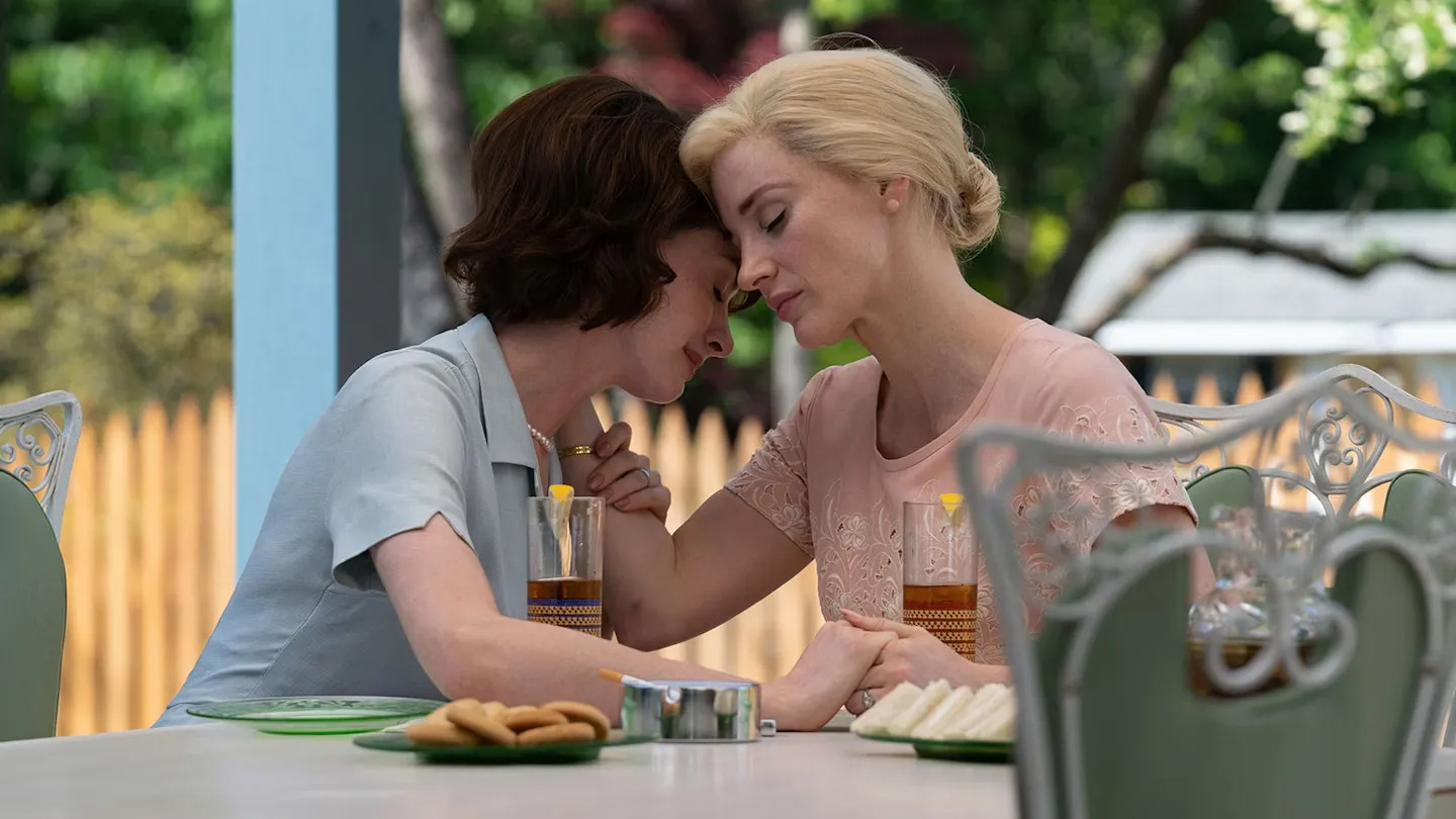 A still from the movie Mother's Instinct showing Jessica Chastain as Alice and Anne Hathaway as Céline, embracing at a table