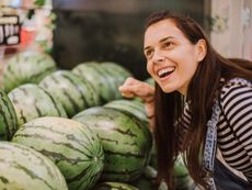 A woman listens as she knocks on a watermelon with her fist
