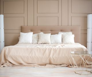 A mattress laden with blankets and pillows against a beige wall.