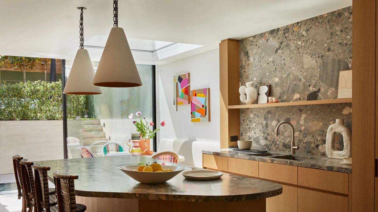 a luxury kitchen extension with brown natural stone surfaces. a skylight sits above a dining area with colorful artwork and vases