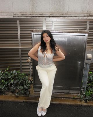 Woman with a sheer lace top, white trousers, and light blue ballet flats