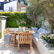 Garden in Fulham, paved with raised beds, wooden table, chairs and inbuilt seat with striped cushions. Susan and Henry Parker's garden at their four bedroom Victorian house in Fulham, London.