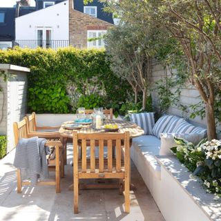 Garden in Fulham, paved with raised beds, wooden table, chairs and inbuilt seat with striped cushions. Susan and Henry Parker's garden at their four bedroom Victorian house in Fulham, London.