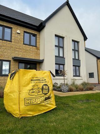 A yellow bag of DIY supplies on a lawn in front of a house