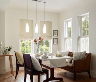 Bright dining corner with white walls, natural daylight from multi windows, and mixed bench and chair seating, with scatter pillows for added comfort.