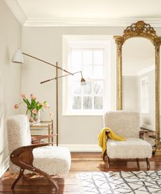 Neutral Living Room with teddy chairs wooden accents, tall brass mirror, lantern with lamps on movable arms and a large bright crittal window facing a winter barren tree