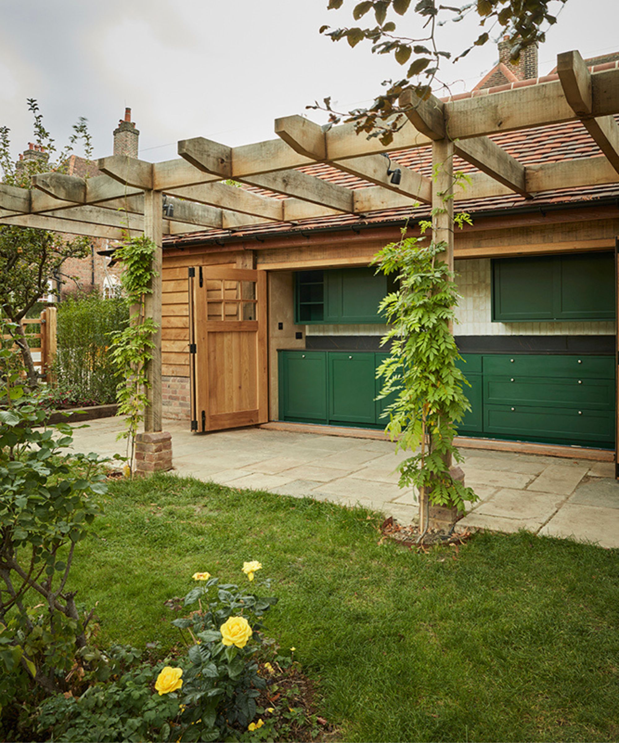 a cottage garden in Hampstead, London with a large green outdoor kitchen under a wooden pergola