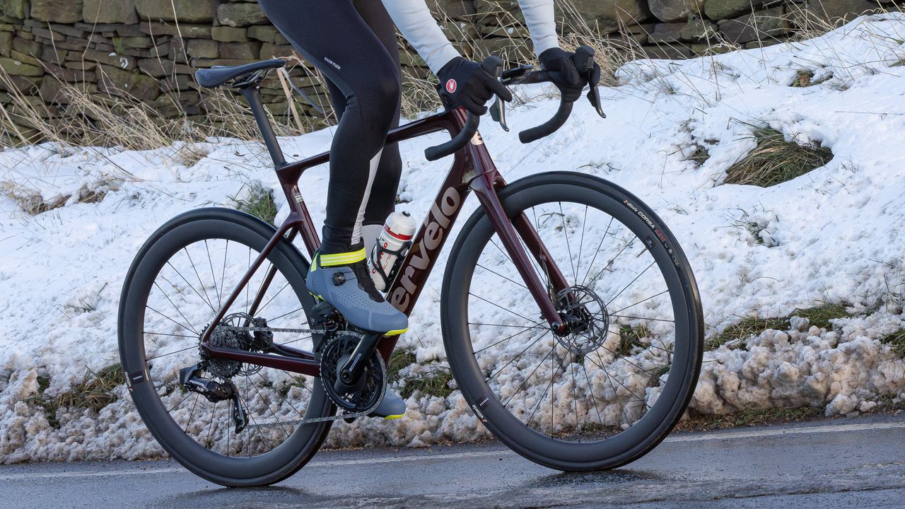 Cervelo Caledonia-5 being ridden up a snowy lane by a male rider wearing a pair of the best winter cycling shoes