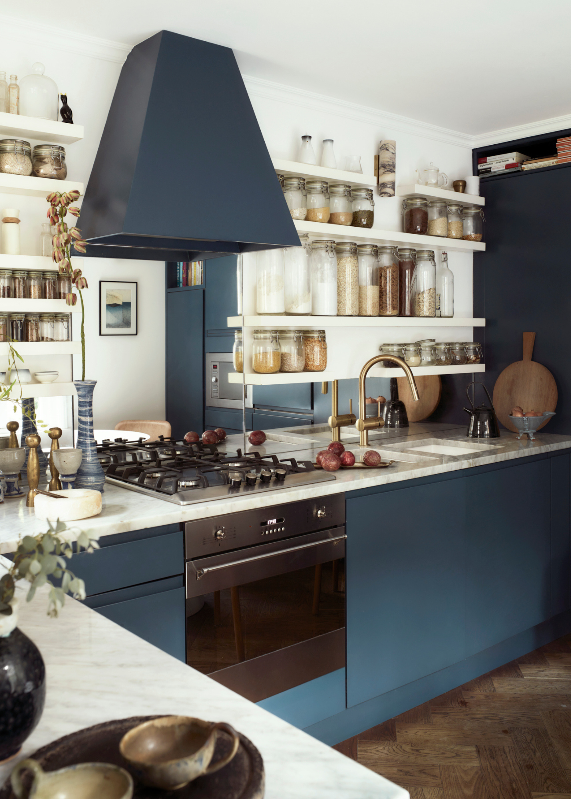 A blue kitchen with white floating shelves and rows of glass jars containing spices and other cooking ingredients.