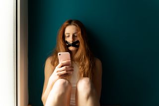 A young woman with tape on her mouth using a smartphone.