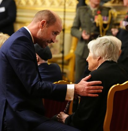 Prince William kneeling and putting his hand on an elderly woman's shoulder