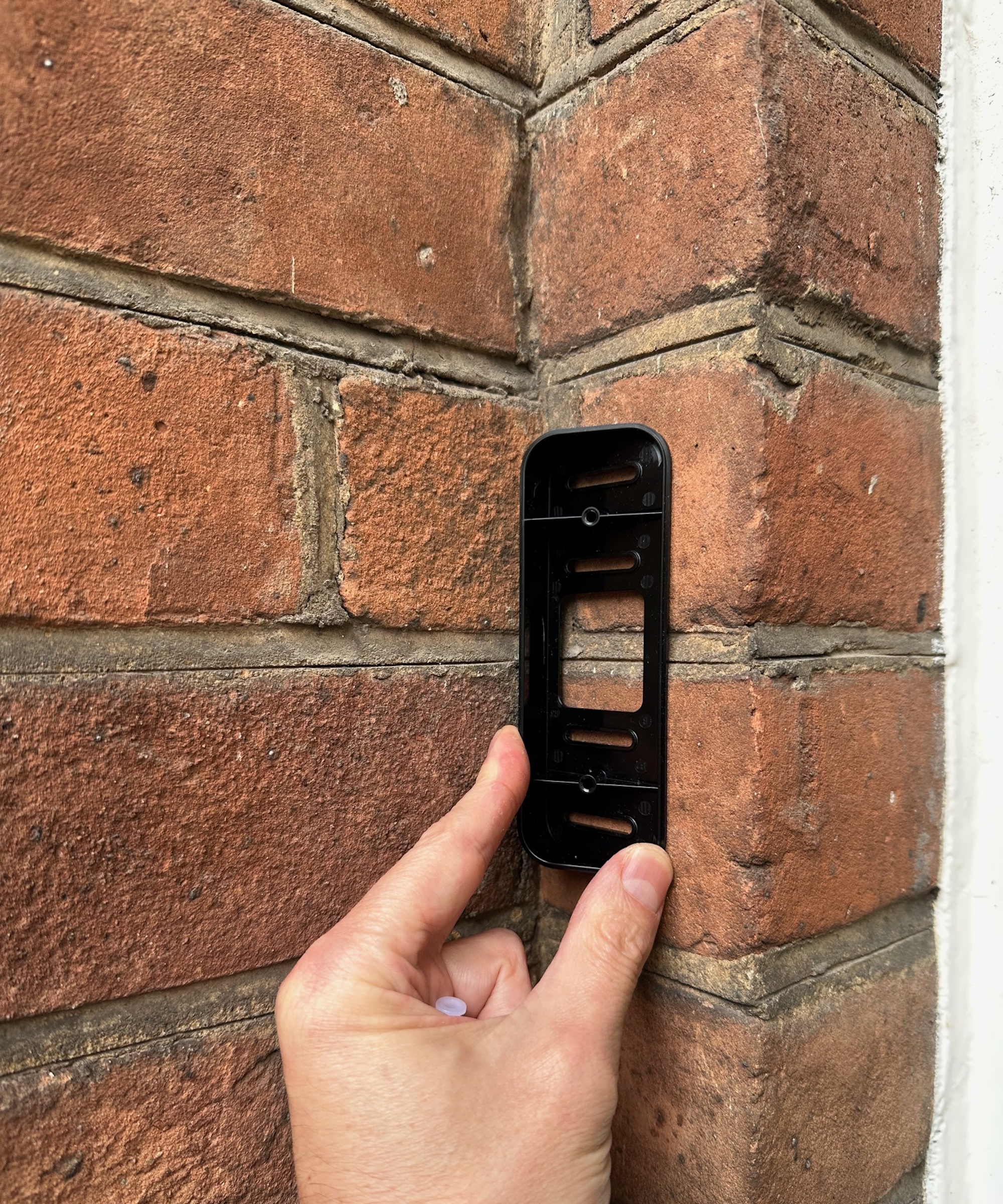 Hand holding corner bracket for Blink video doorbell against brick wall