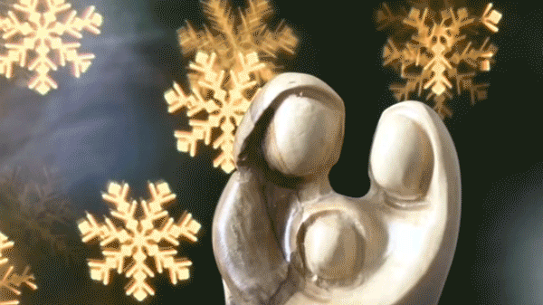Spinning, snowflake-shaped "bokeh balls" behind a carved wooden nativity figurine