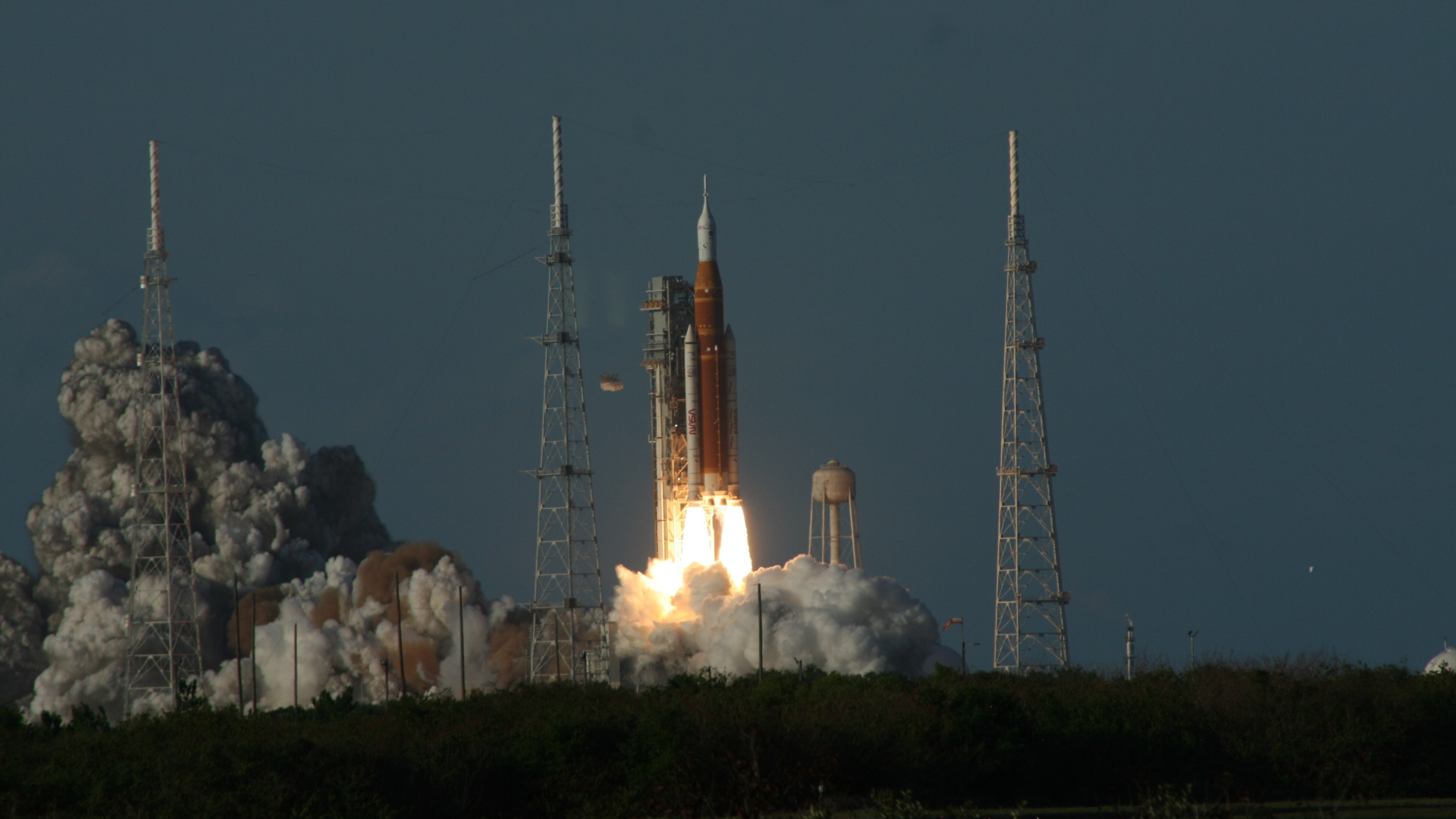 An orange and white rocket blasts off a launchpad, billowing gray smoke behind it
