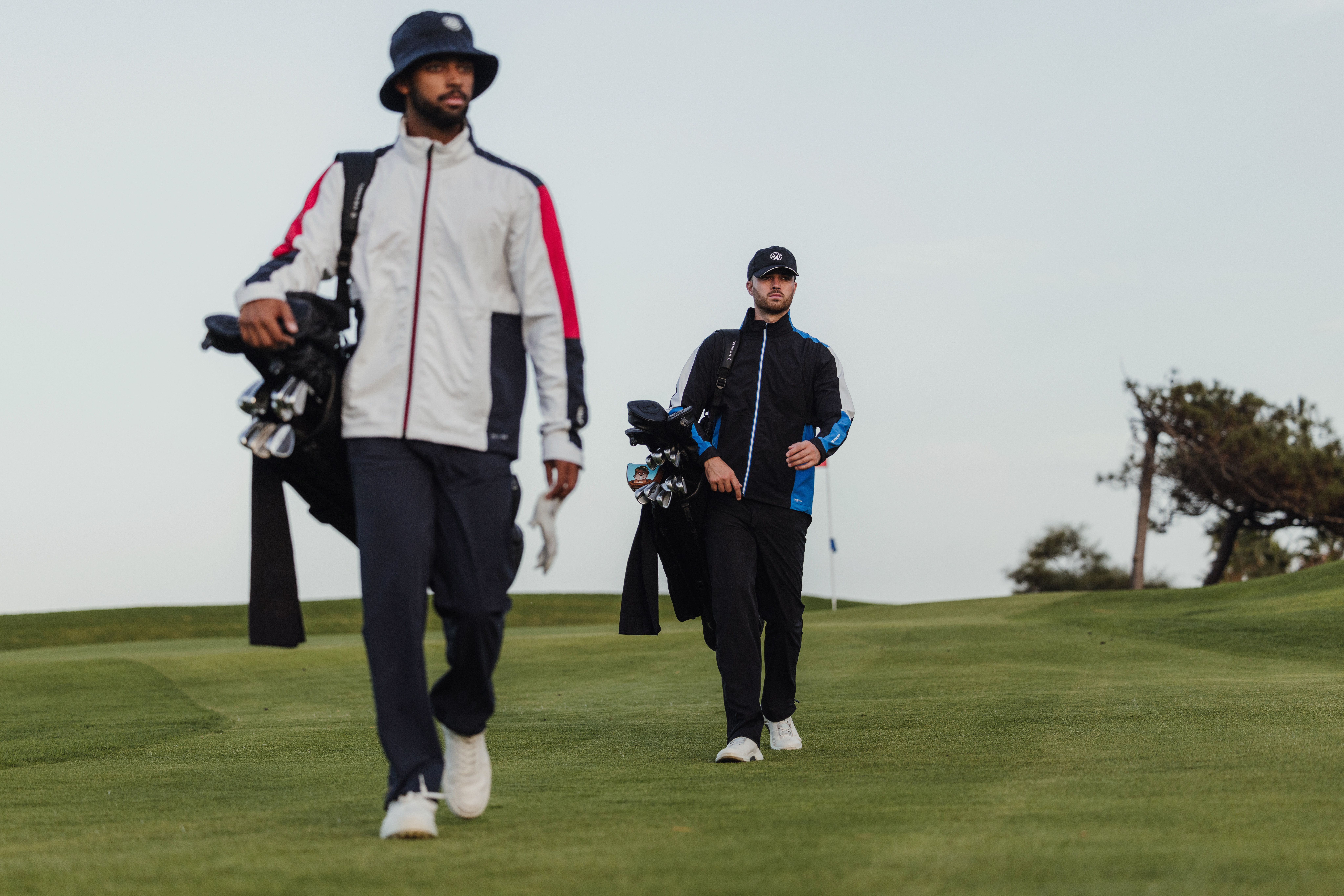 Two golfers walking on a fairway carrying their bags wearing rain gear