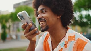 A photo of a man holding an iPhone in front of his face and talking into it. He has a happy expression on his face.