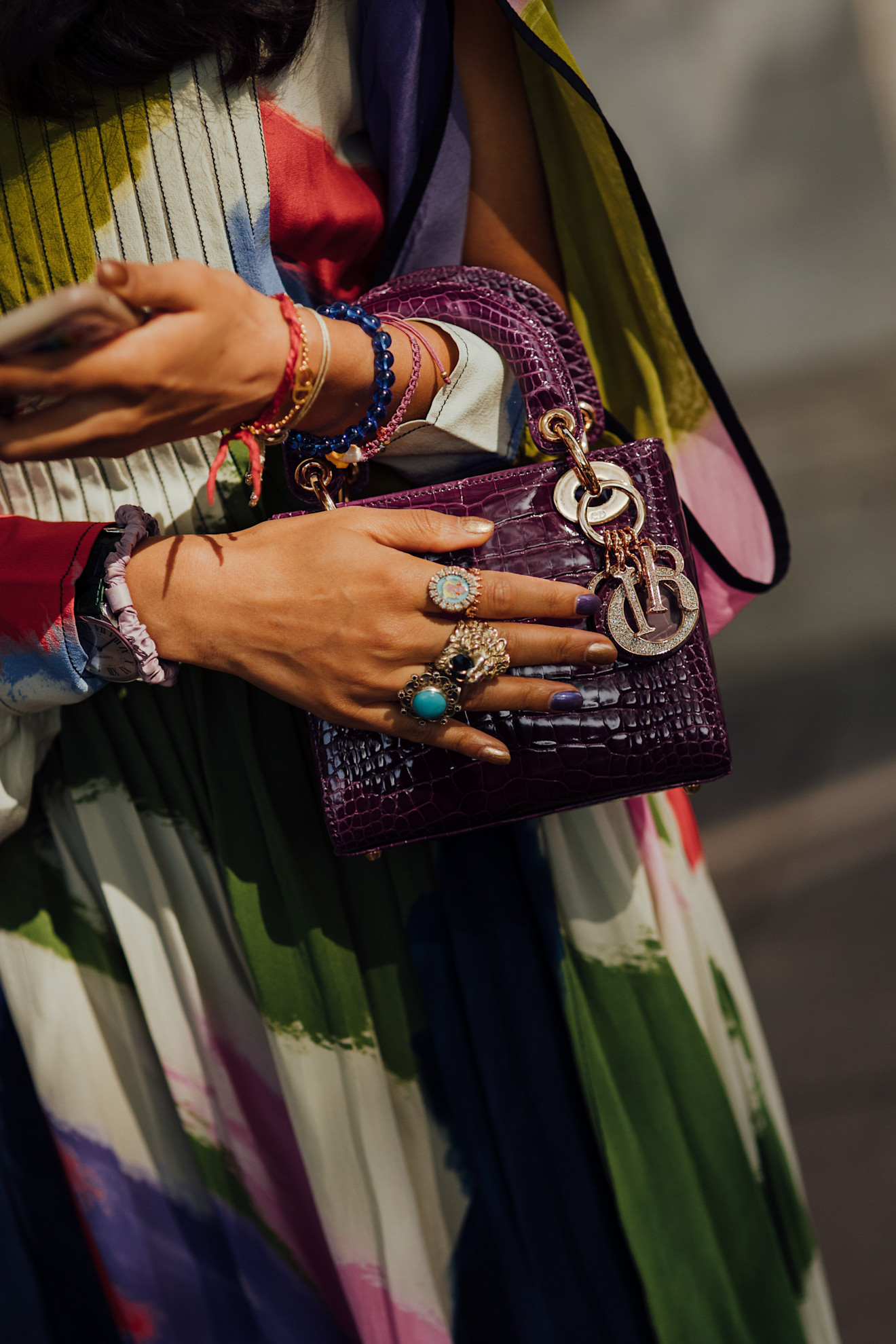 a close up of a woman's blue and gold nails and colorful skirt with a purple dior bag