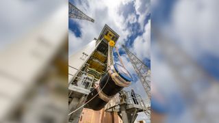 A large black cylinder is raised on a crane. 