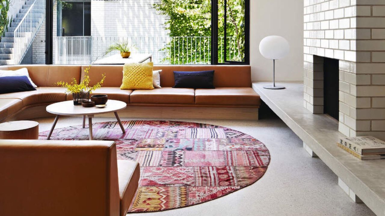 A mid-century modern living room with low tanned modular seating and a large stone fireplace and round colorful rug