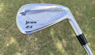 The Srixon ZX4 Mk II Iron held aloft, showing off its very cool, chiseled clubhead on a grassy background