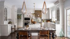 A white kitchen with classic shaker cabinets, a copper range hood, a wooden table, and marble countertops