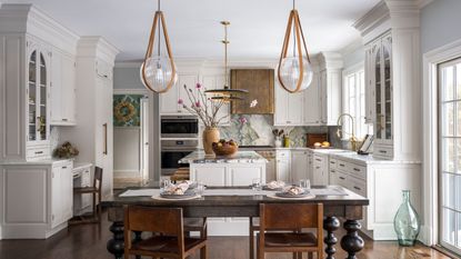 A white kitchen with classic shaker cabinets, a copper range hood, a wooden table, and marble countertops