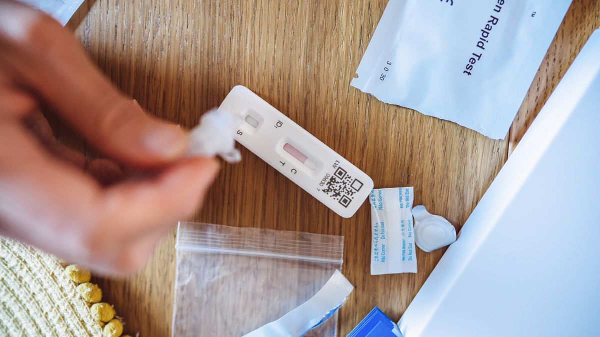 A woman squeezing liquid solution from an at-home COVID-19 test onto a test strip.